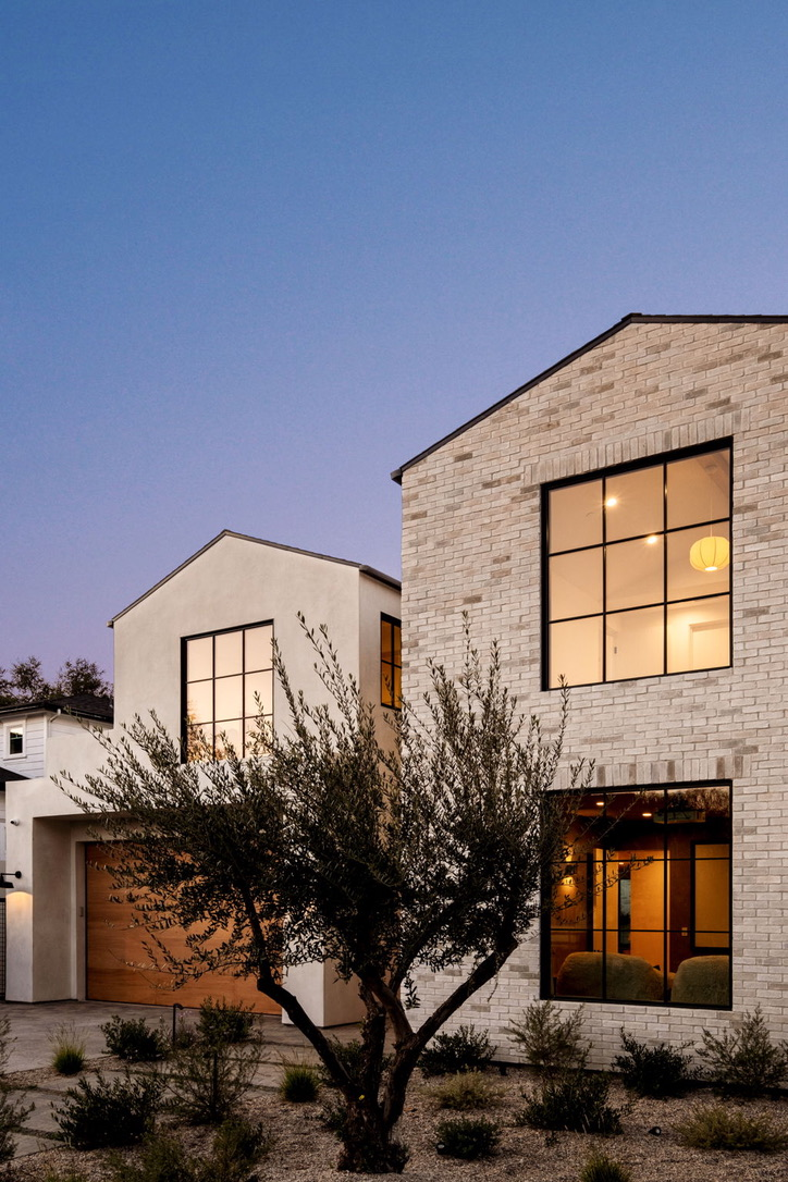 White brick and stucco two-storey home at dusk with olive tree and oak garage door