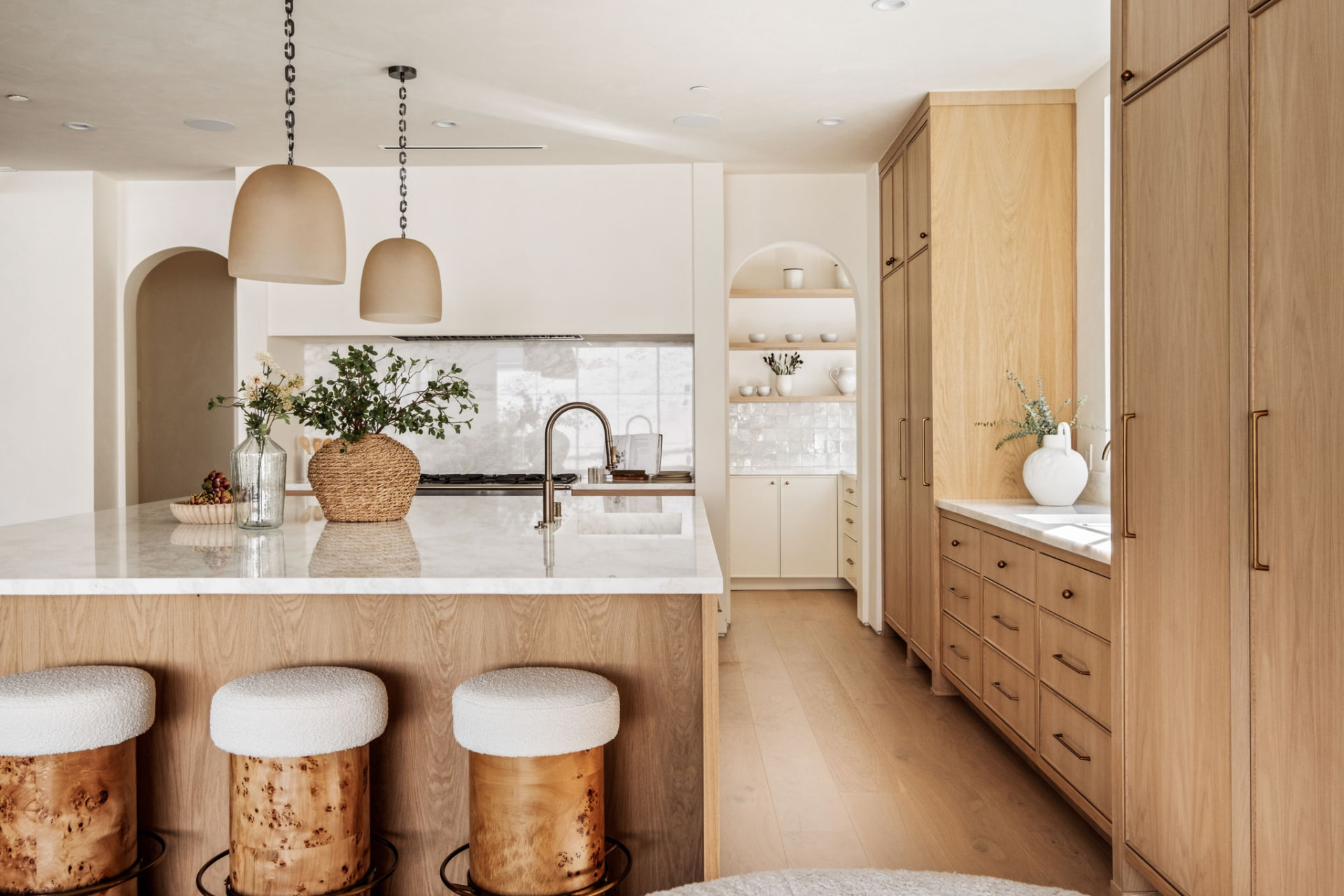 White oak kitchen with marble island, arched pantry nook and bouclé counter stools