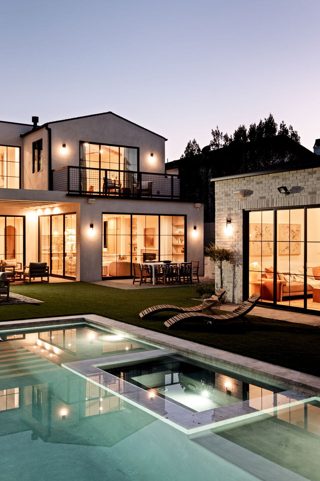 Modern Spanish residence at dusk with lit steel windows, pool and brick guest house