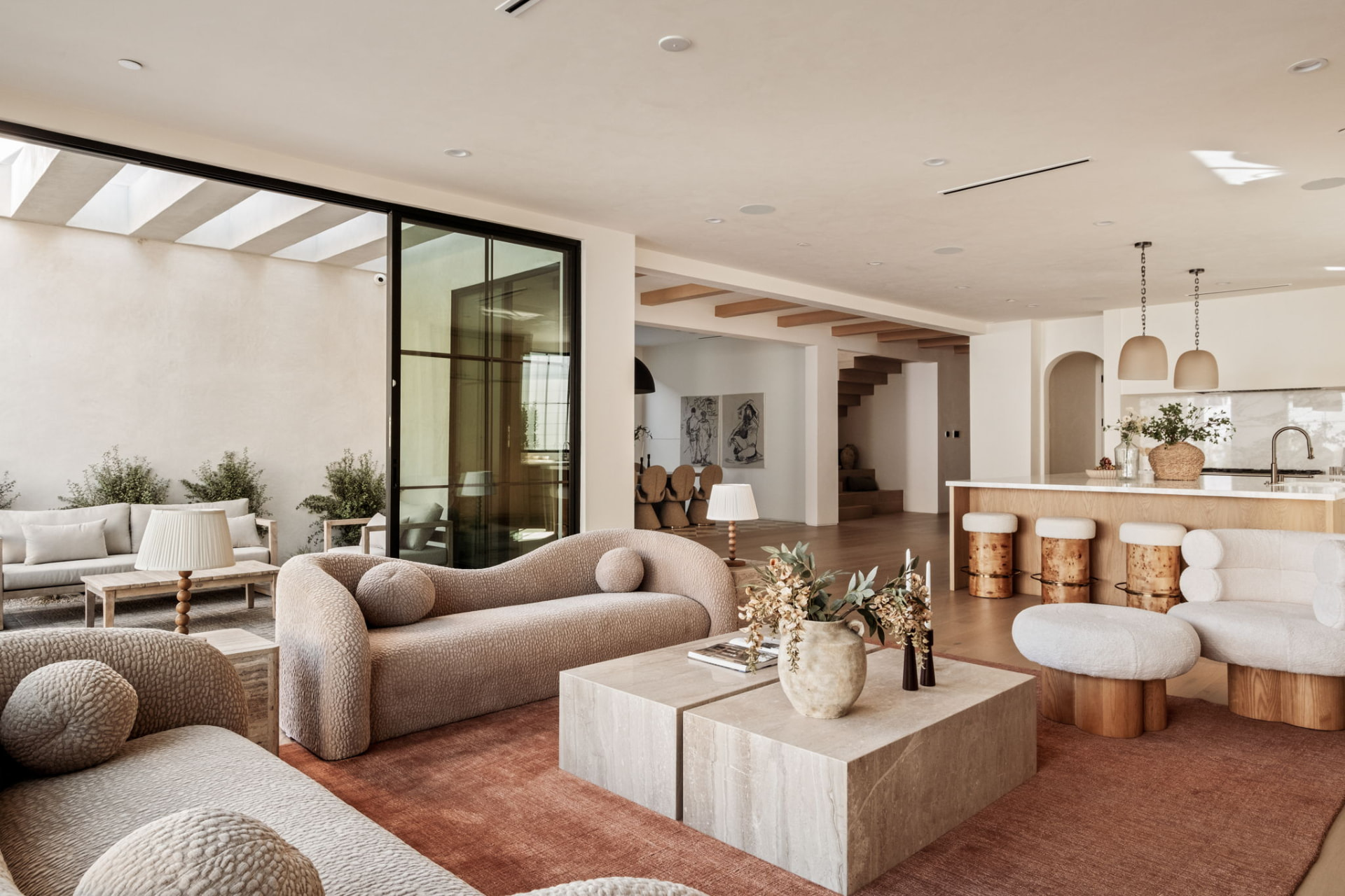 Great room connecting lounge, kitchen island and courtyard with oak beams, terracotta rug and travertine coffee tables