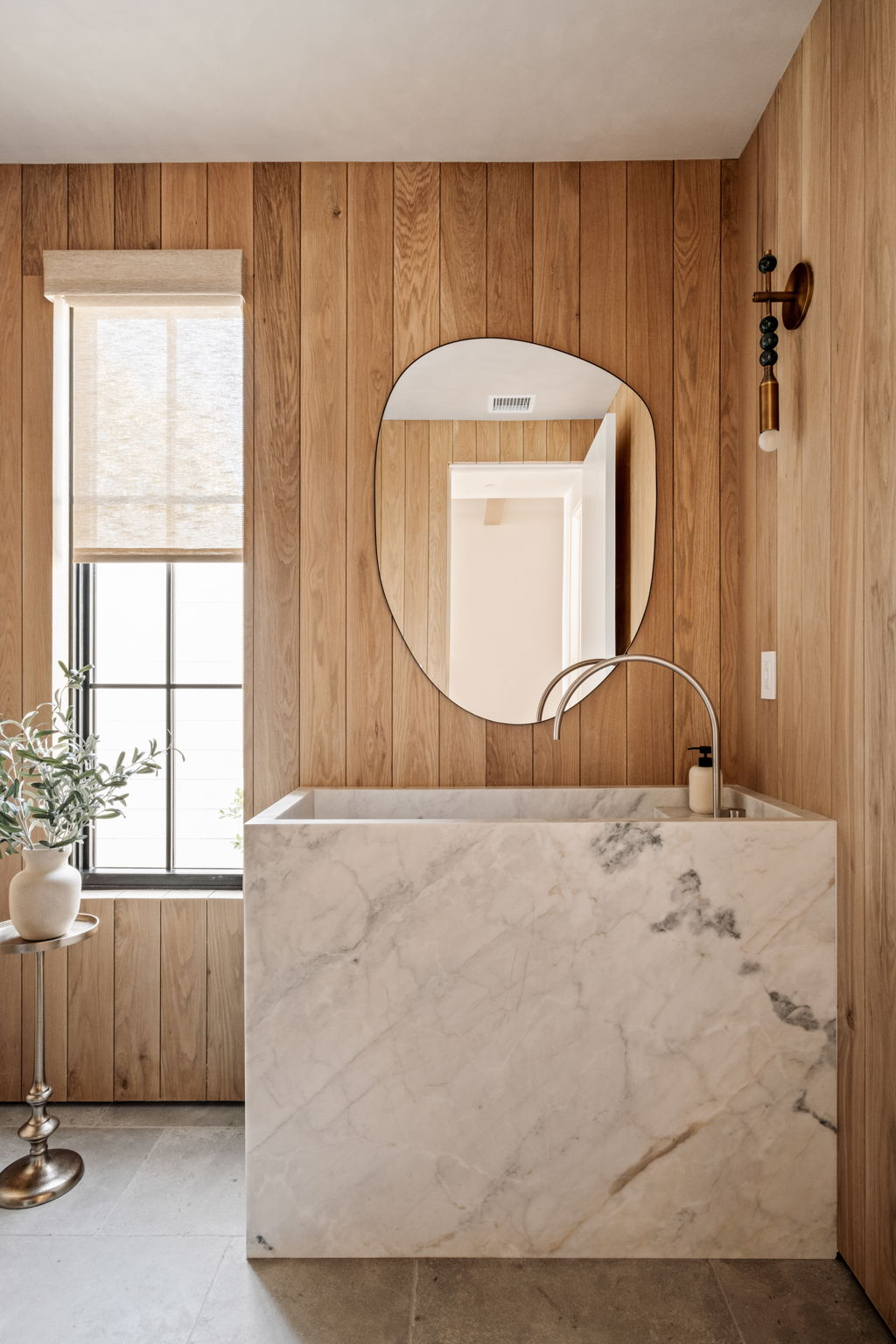 Powder room with white oak paneling, marble monolith sink and organic mirror