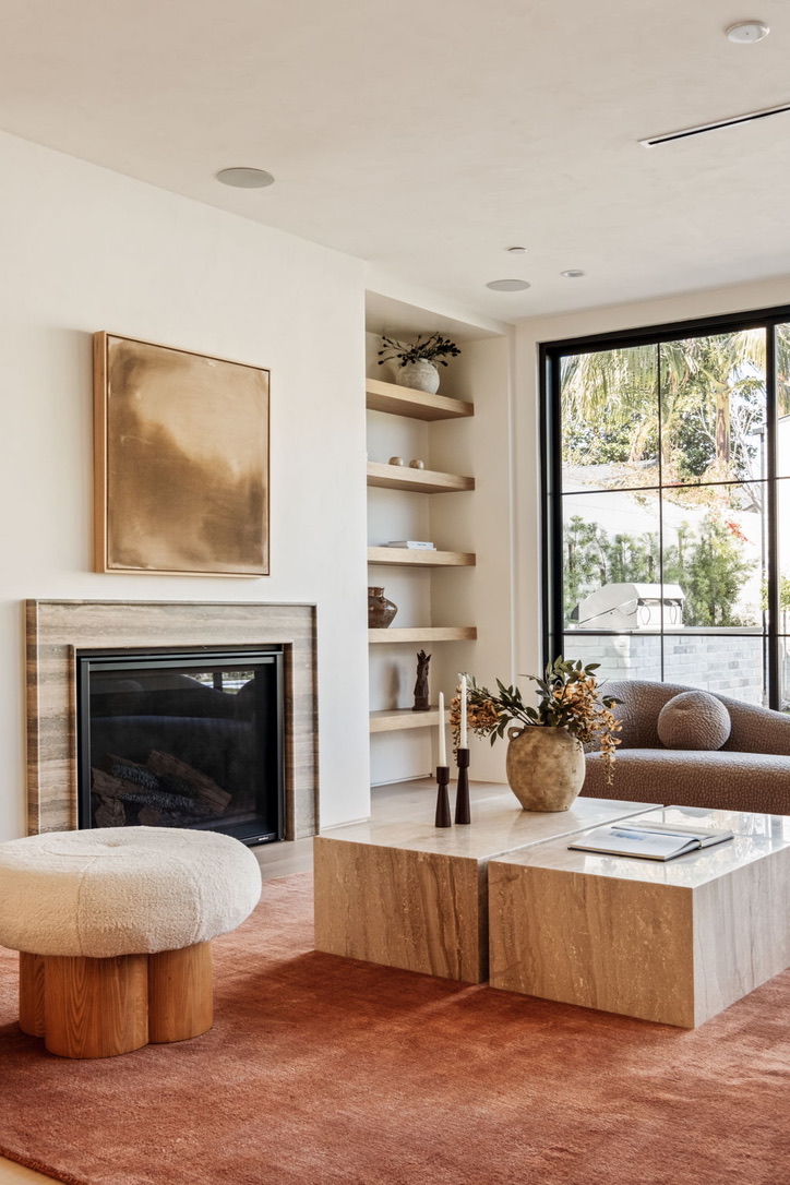 Close view of a travertine fireplace surround, brass artwork, layered oak shelving and a black steel picture window